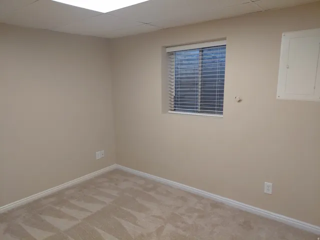Recessed ceiling lighting with a drop ceiling, single window with blinds, light-toned wall paint, and patterned carpet flooring