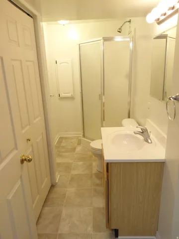 Bathroom featuring a corner shower with a glass enclosure, wood-finish vanity with an integrated sink, and square tile flooring
