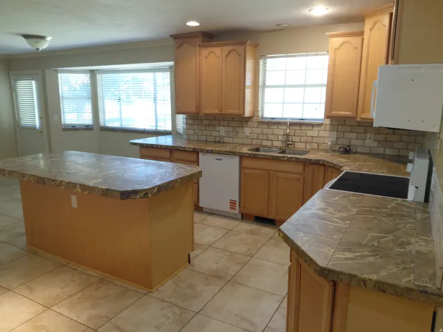 Kitchen featuring a central island, wood-finish cabinetry, tile flooring, and a tiled backsplash