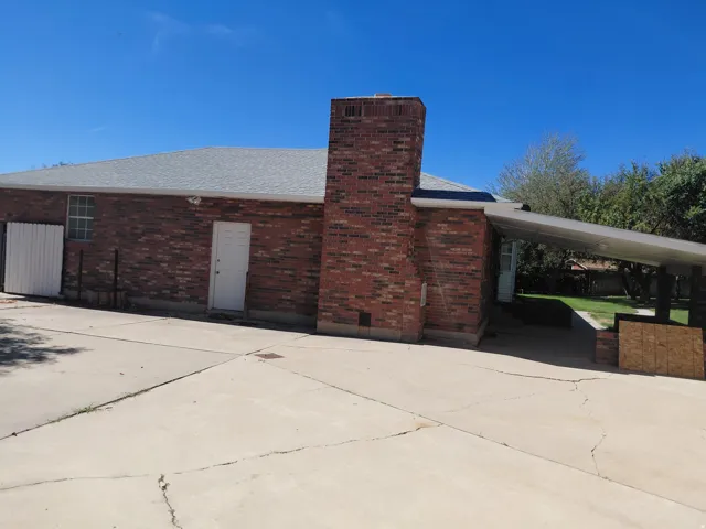 Brick exterior with a prominent chimney, a white exterior door, a multi-pane window, and a covered carport with a flat roof
