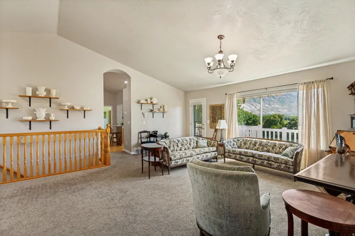 Vaulted ceiling, arched doorway, wood railing, chandelier, and sliding glass door leading to an outdoor space