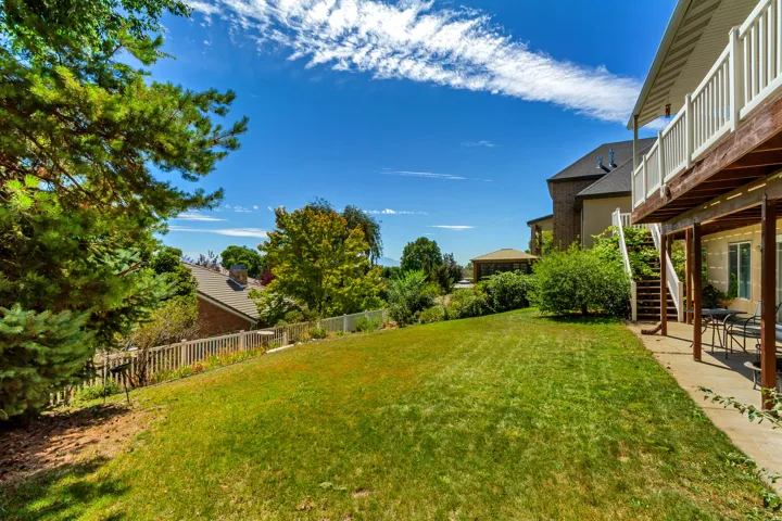 Expansive sloped lawn with surrounding mature trees, a concrete patio, and an upper-level deck with white railings