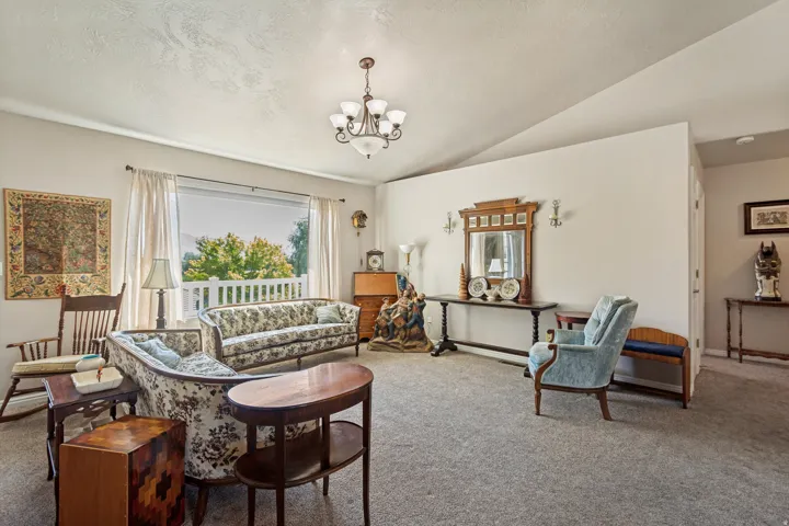 Vaulted ceiling with an overhead chandelier, large window with outdoor railing, wall-mounted sconces, and neutral carpeting