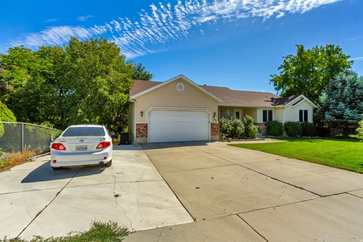 Stucco exterior with brick accents, attached garage, concrete driveway, front lawn, and mature trees