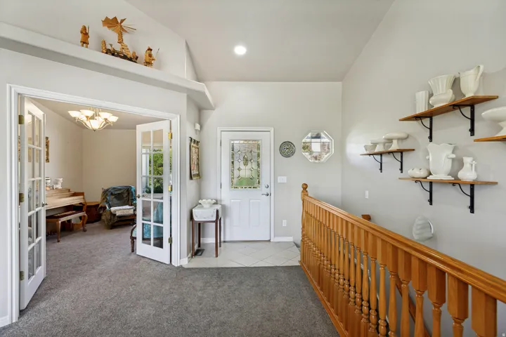 Vaulted ceiling, glass-paneled entry door, wood-finish railing, and double French doors opening to an additional room