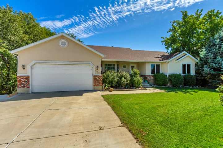 Stucco exterior with brick detailing, attached two-car garage, mature landscaping, and concrete driveway