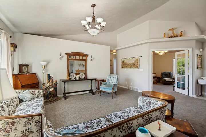Vaulted ceiling, chandelier lighting, wall sconces, carpet flooring, and French doors