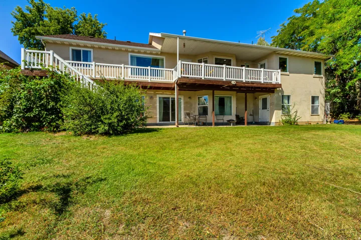 Expansive rear yard with a manicured lawn, tiered deck with white railings, and a lower-level patio