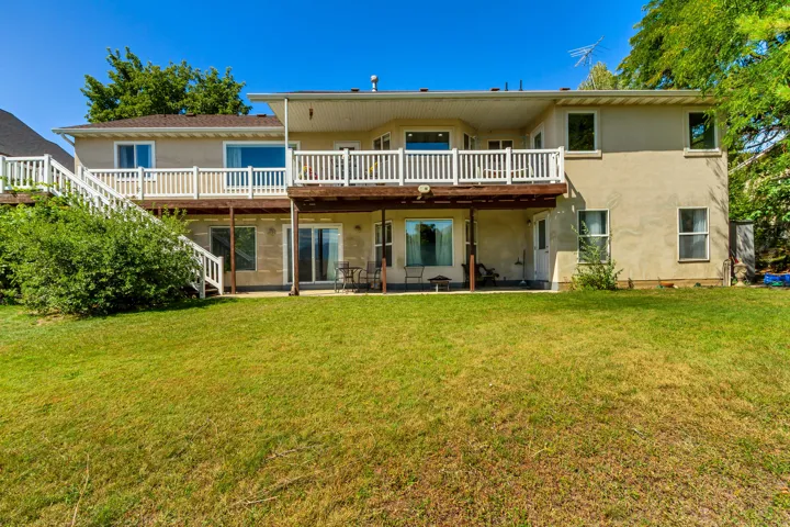Expansive green lawn with a multi-level deck featuring white railings and a covered patio area