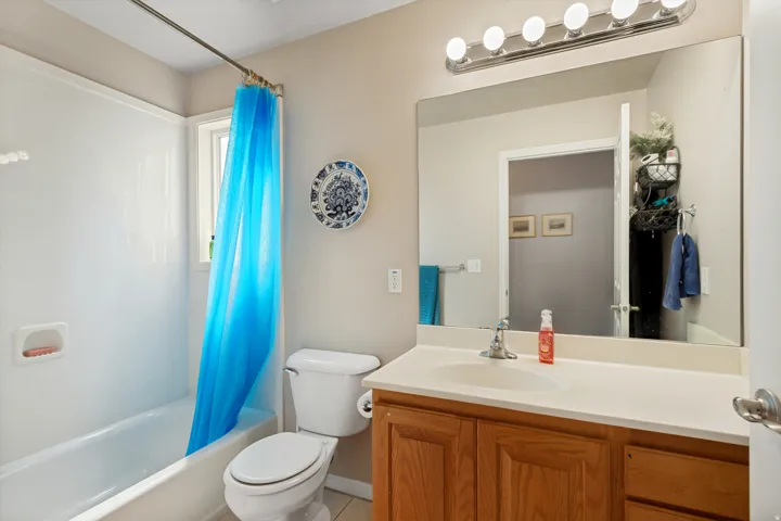 Bathroom featuring a built-in tub with shower, wood-finish vanity with an integrated sink, broad wall mirror, and a five-bulb vanity light fixture