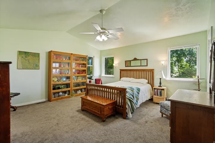 Vaulted ceiling with a ceiling fan, carpeted flooring, and multiple windows