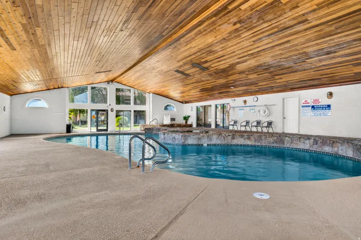 Indoor swimming pool with a wood-paneled vaulted ceiling, expansive window walls, and a stone-clad hot tub