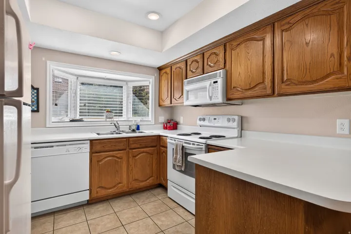 Kitchen featuring wood cabinetry, white appliances, a bay window, recessed lighting, and tile flooring