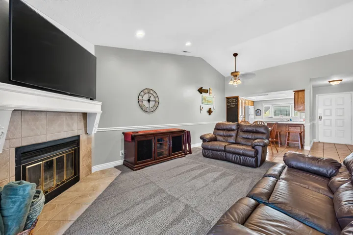 Vaulted ceiling, tiled fireplace with mantel, recessed lighting, crown molding, and an open-concept layout to the kitchen