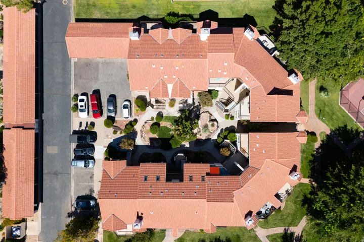Terracotta tile roofing, central courtyard, mature landscaping, paved parking area, and surrounding green spaces