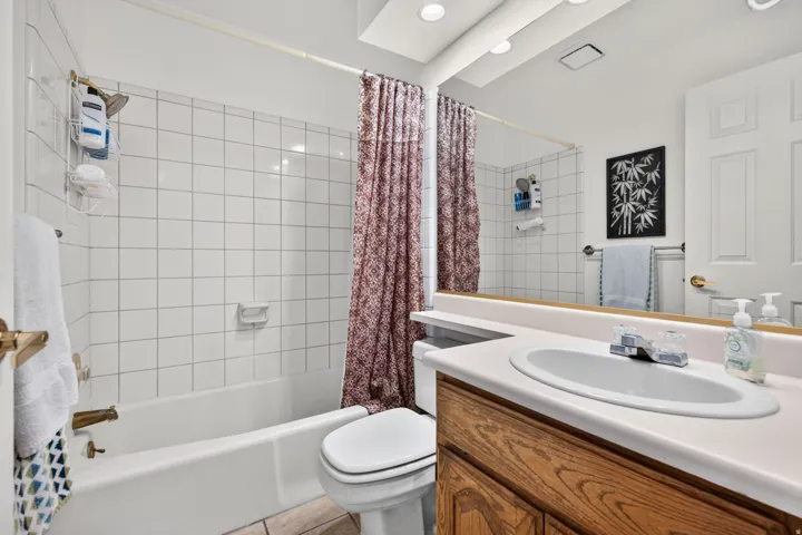 Bathroom featuring a built-in tub with white tile surround, a wood-finish vanity with an integrated sink, and an overhead lighting fixture