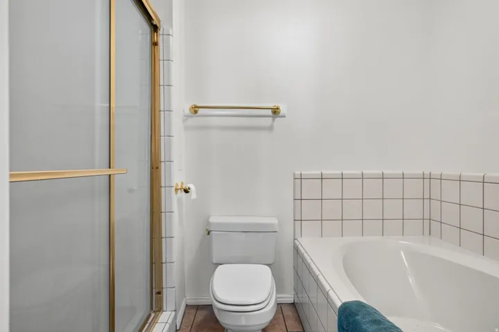 Gold-finish framed shower enclosure, white ceramic tiled tub surround, and a built-in soaking tub