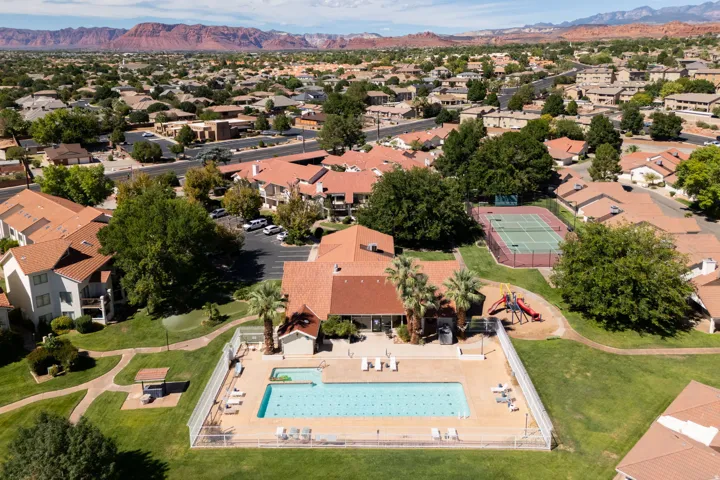 Community pool with a surrounding fence, tennis courts, and a playground structure on a grass expanse