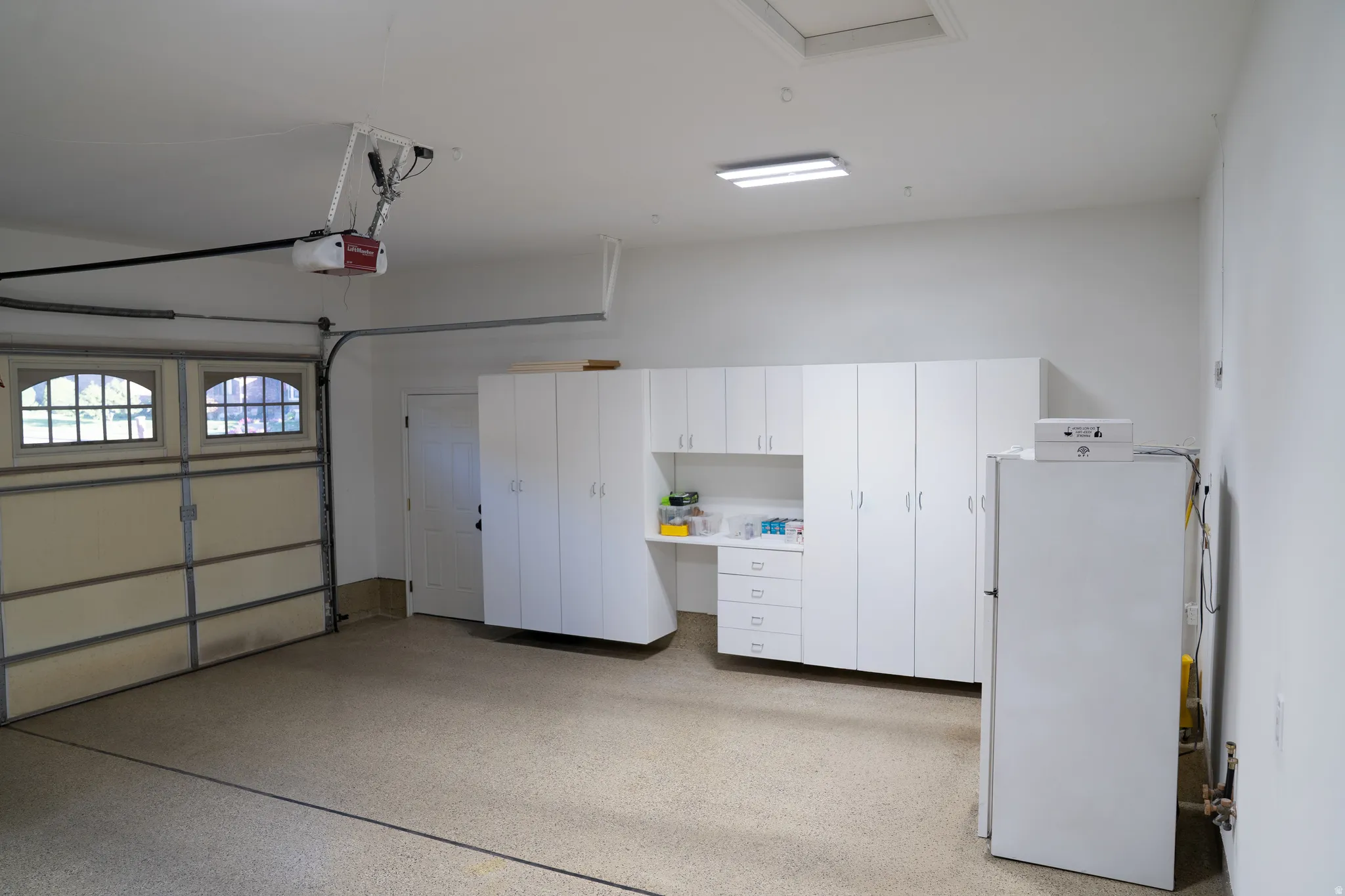 Spacious garage featuring a durable epoxy floor, comprehensive built-in white cabinetry, a dedicated workbench area, and an interior access door