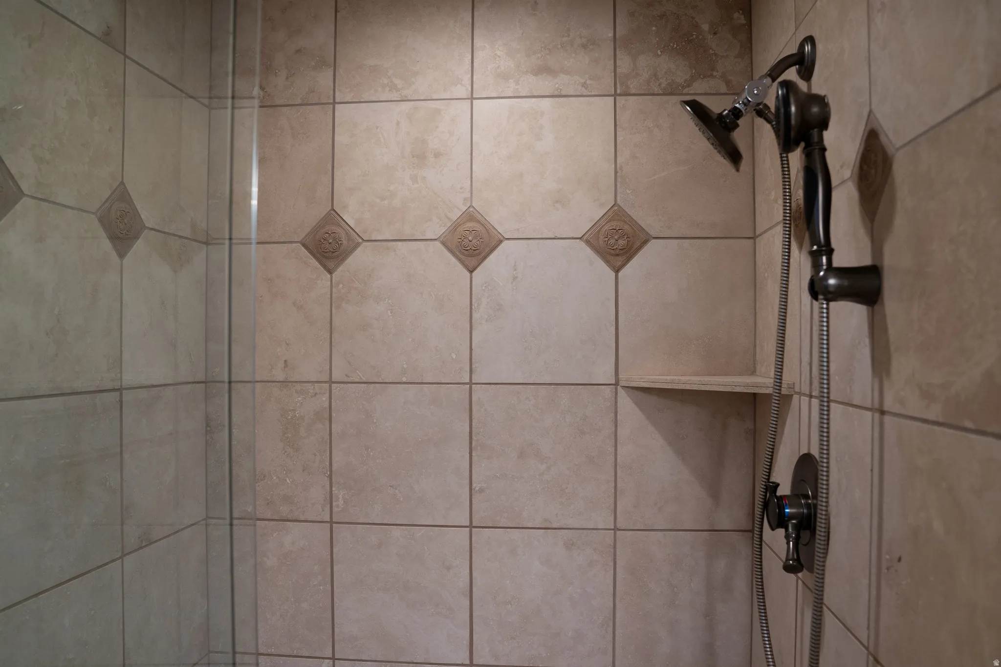 Tiled shower surround featuring decorative accent tiles and a built-in corner shelf
