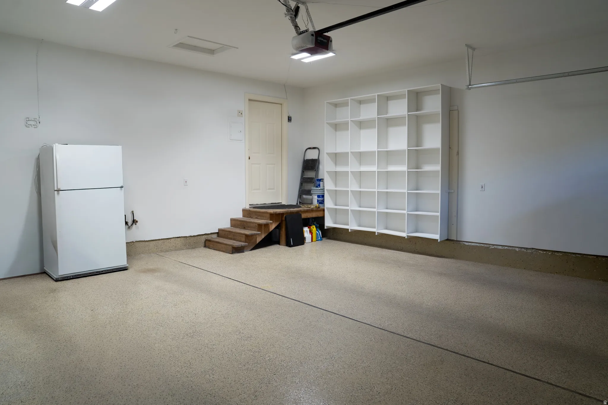 Spacious garage with light-colored epoxy flooring, built-in shelving, and direct access door