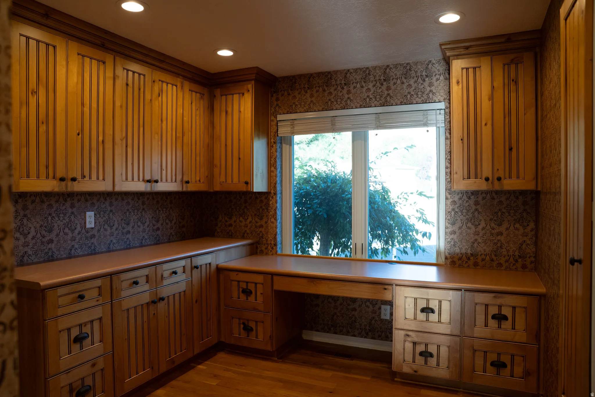Built-in wood cabinetry with black hardware, wood-finish flooring, recessed lighting, and a large window