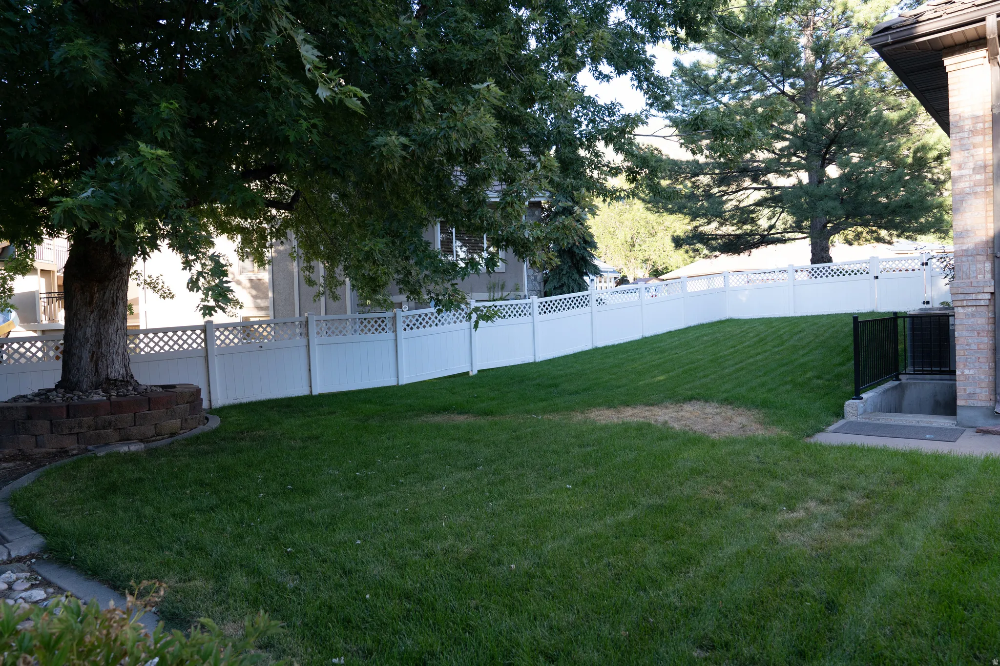 Expansive grassy area with a white lattice-top fence and mature trees