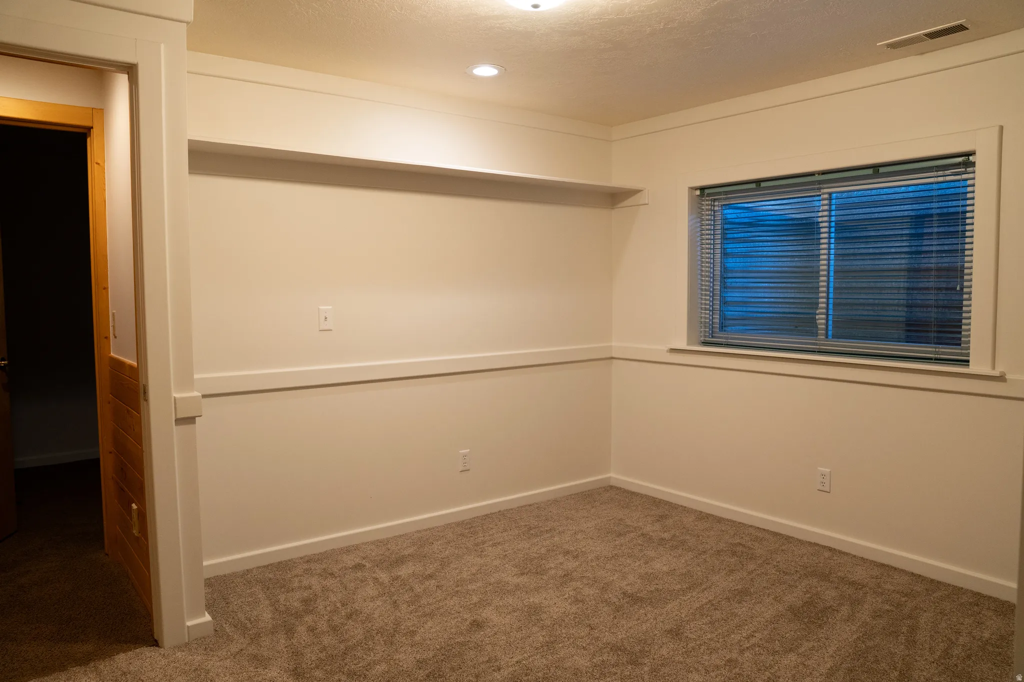 Neutral-toned carpeting, recessed ceiling lighting, a built-in wall shelf, and wood trim detailing