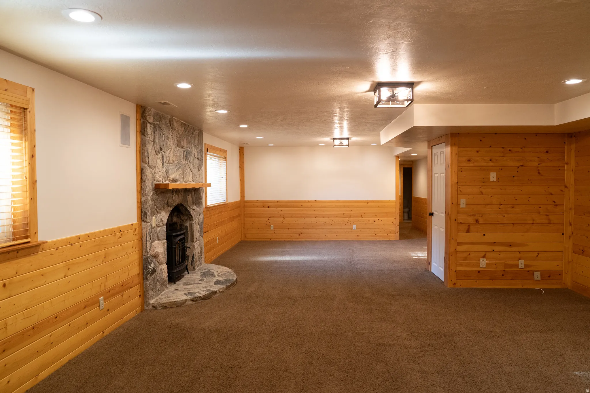 Stone fireplace with hearth and mantel, recessed lighting, wood-finish wainscoting, and a carpeted floor