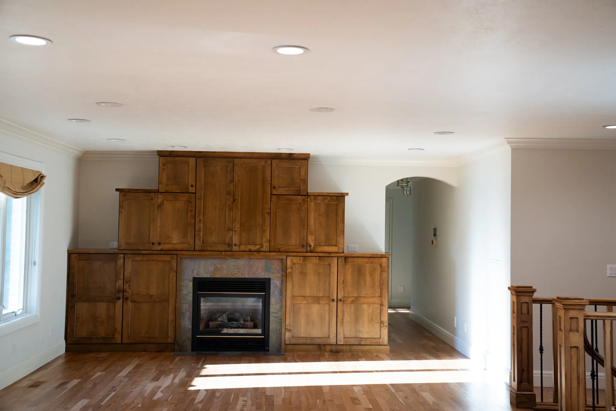 Built-in cabinetry surrounding a fireplace with stone-finish surround, recessed ceiling lighting, wood-finish flooring, and crown molding