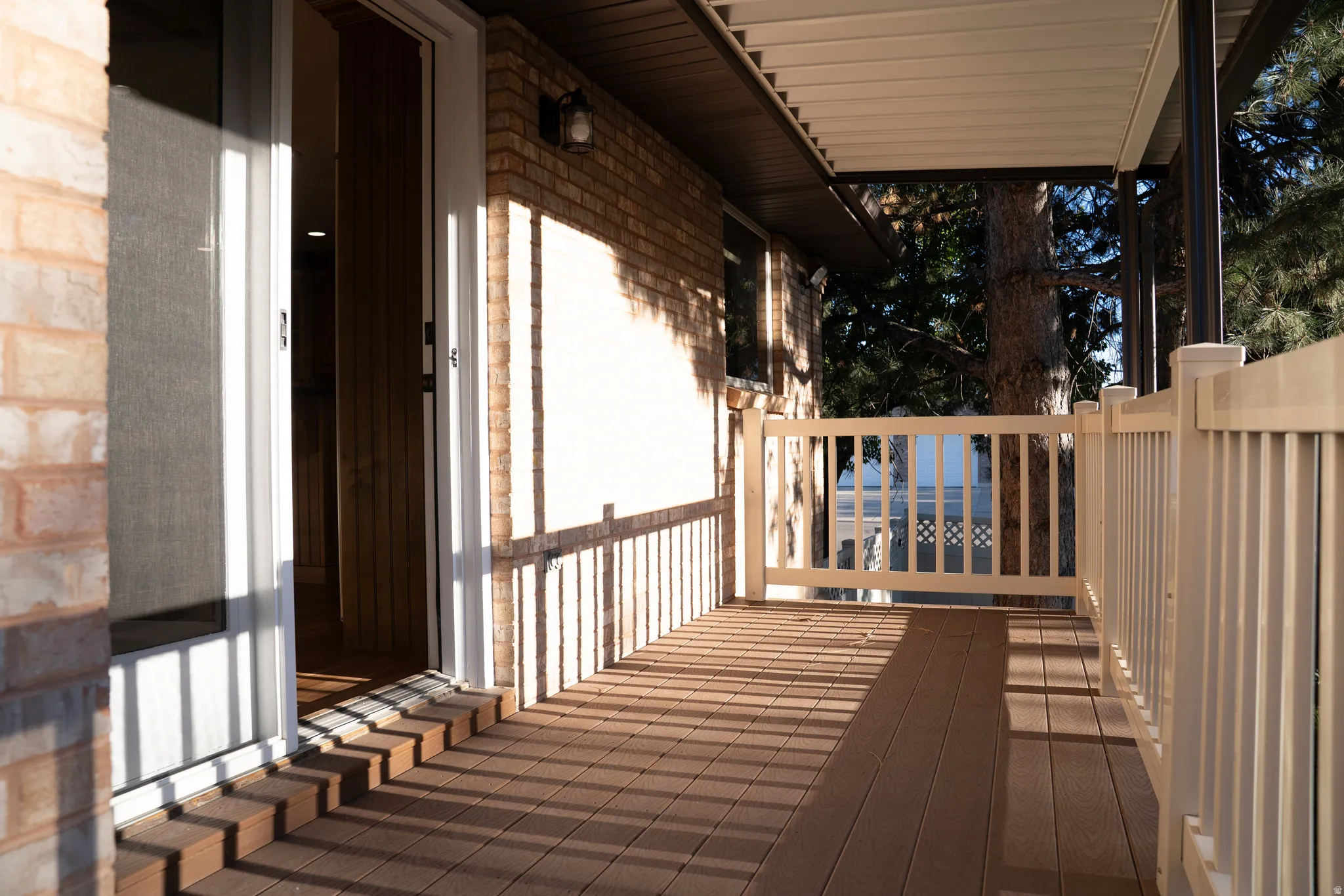 Expansive covered deck featuring composite decking, a white railing system, and brick exterior accents