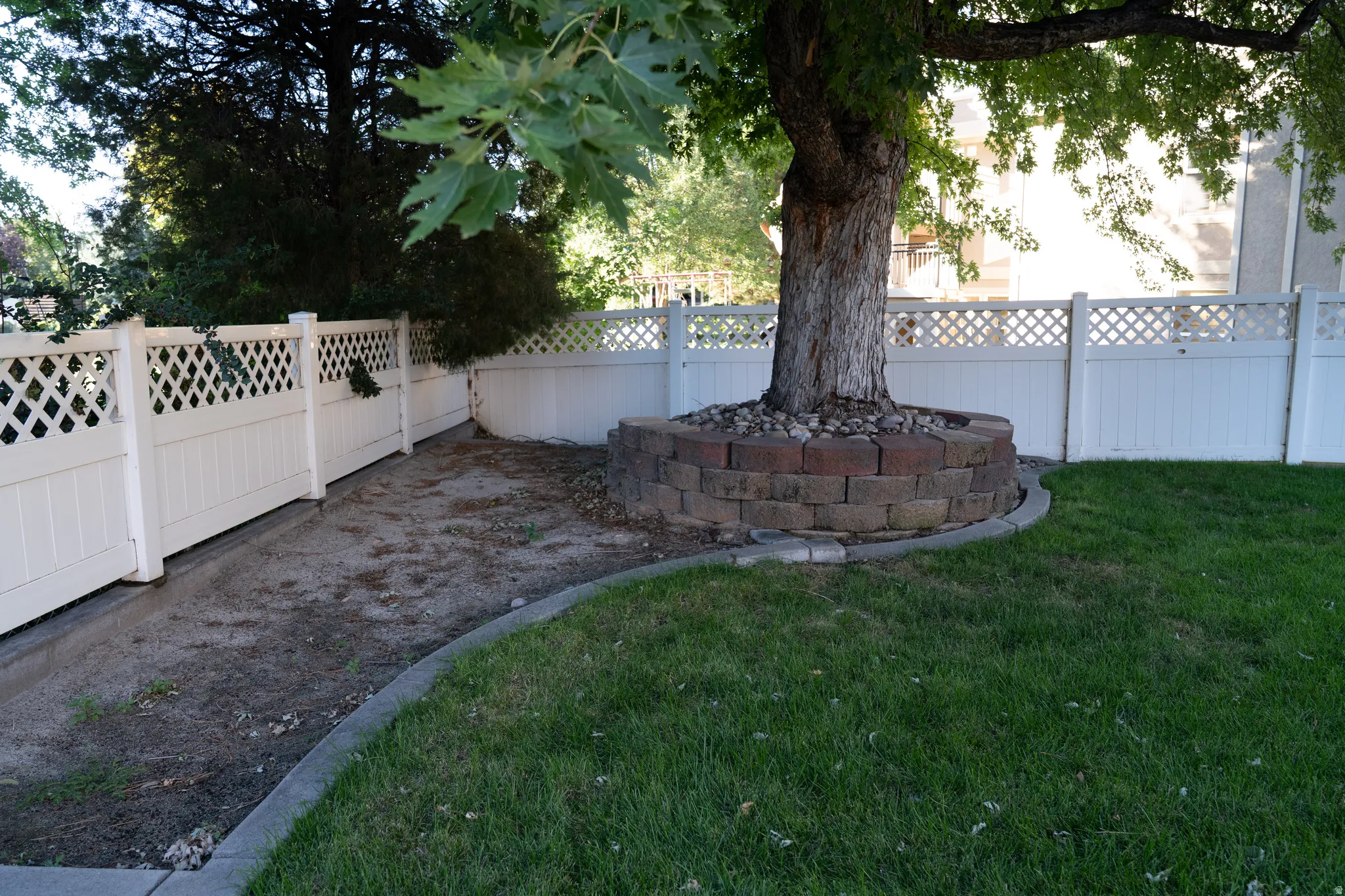 Manicured lawn, mature tree, brick tree surround, concrete curbing, and white lattice fencing
