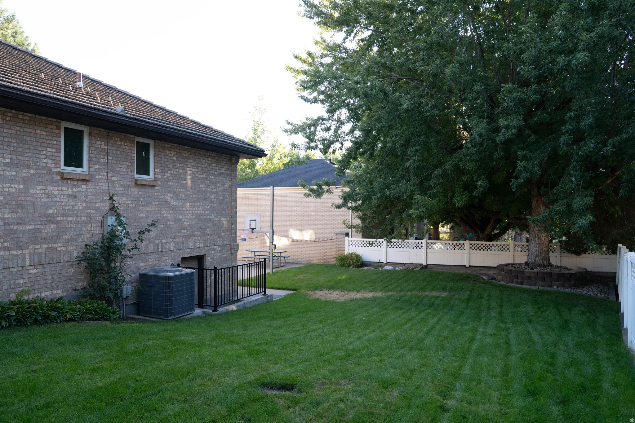 Expansive grassy yard featuring a mature shade tree, brick exterior, and white lattice fencing