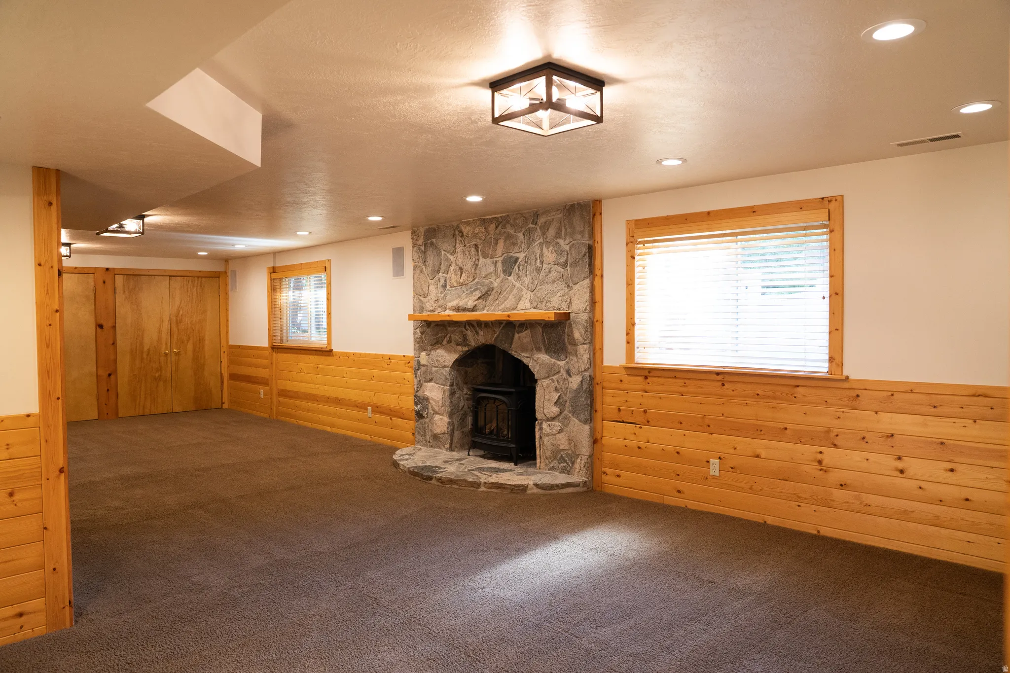 Stone-faced fireplace with wood mantel, wood paneling, recessed lighting, and a neutral carpeted floor