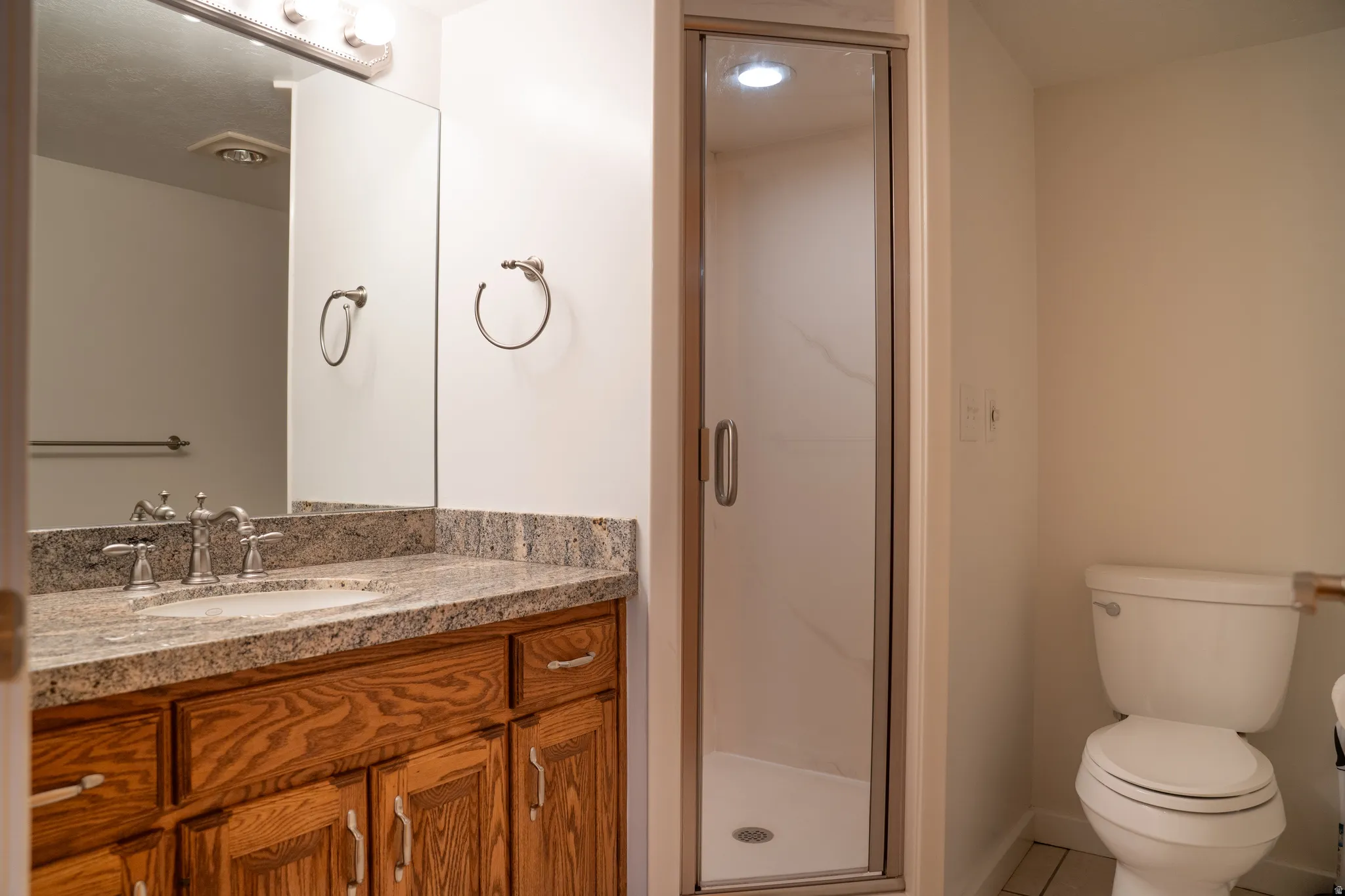 Vanity with granite-style countertop, wood-finish cabinetry, and an undermount sink