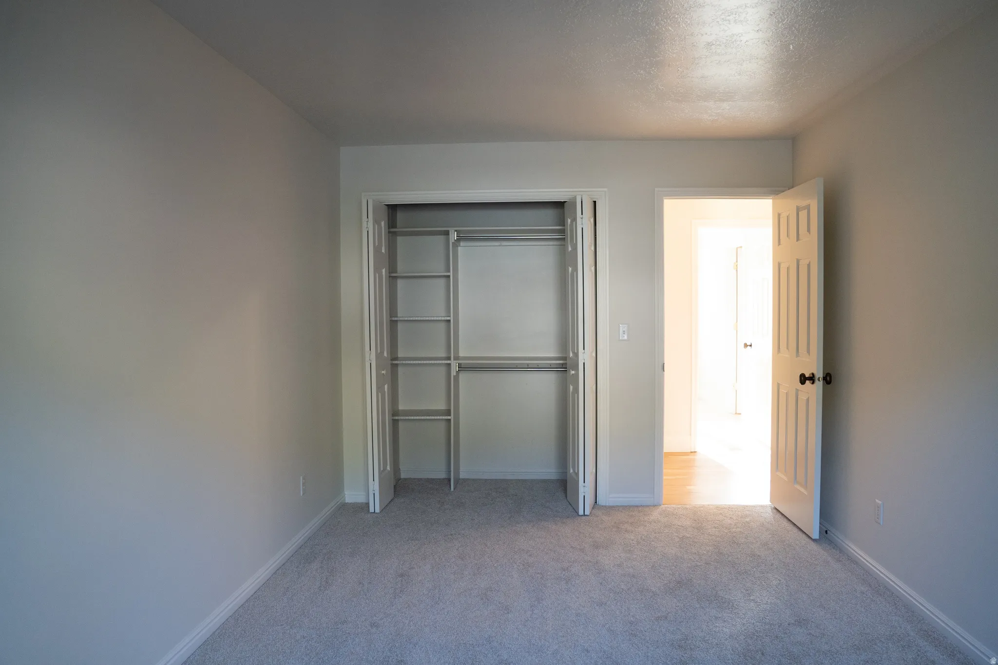 Carpeted room with a closet featuring bi-fold doors and built-in shelving, and a paneled door with dark hardware