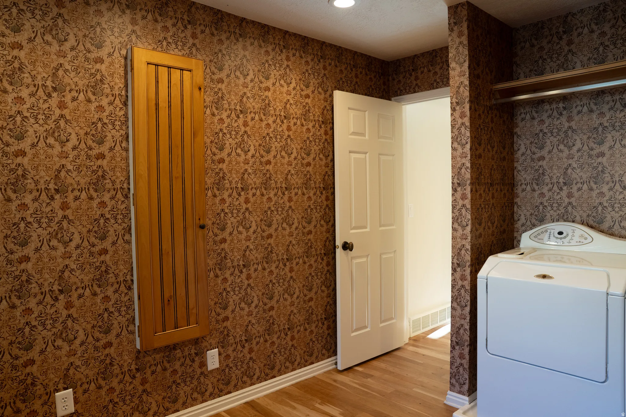 Patterned wallpaper, wood-finish flooring, paneled interior door, built-in shelving, recessed ceiling lighting