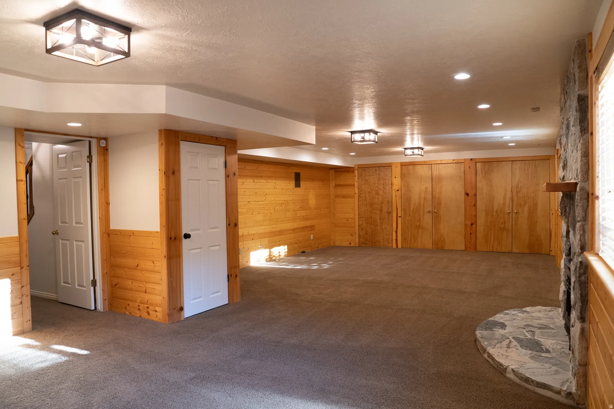 Expansive carpeted room with wood paneling, recessed lighting, and a stone-clad fireplace