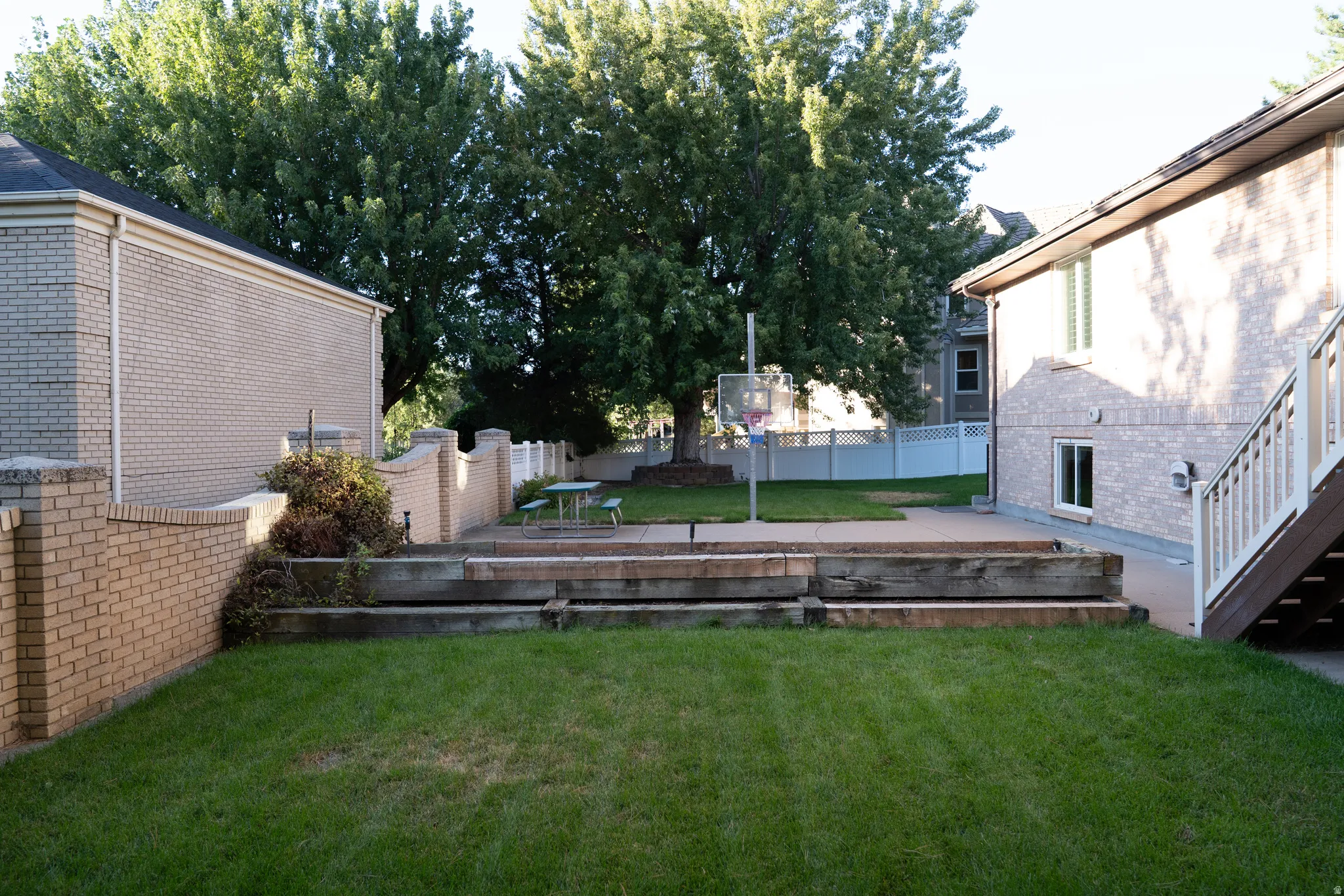 Expansive grassy yard with tiered landscaping, a concrete patio area, and a brick privacy wall