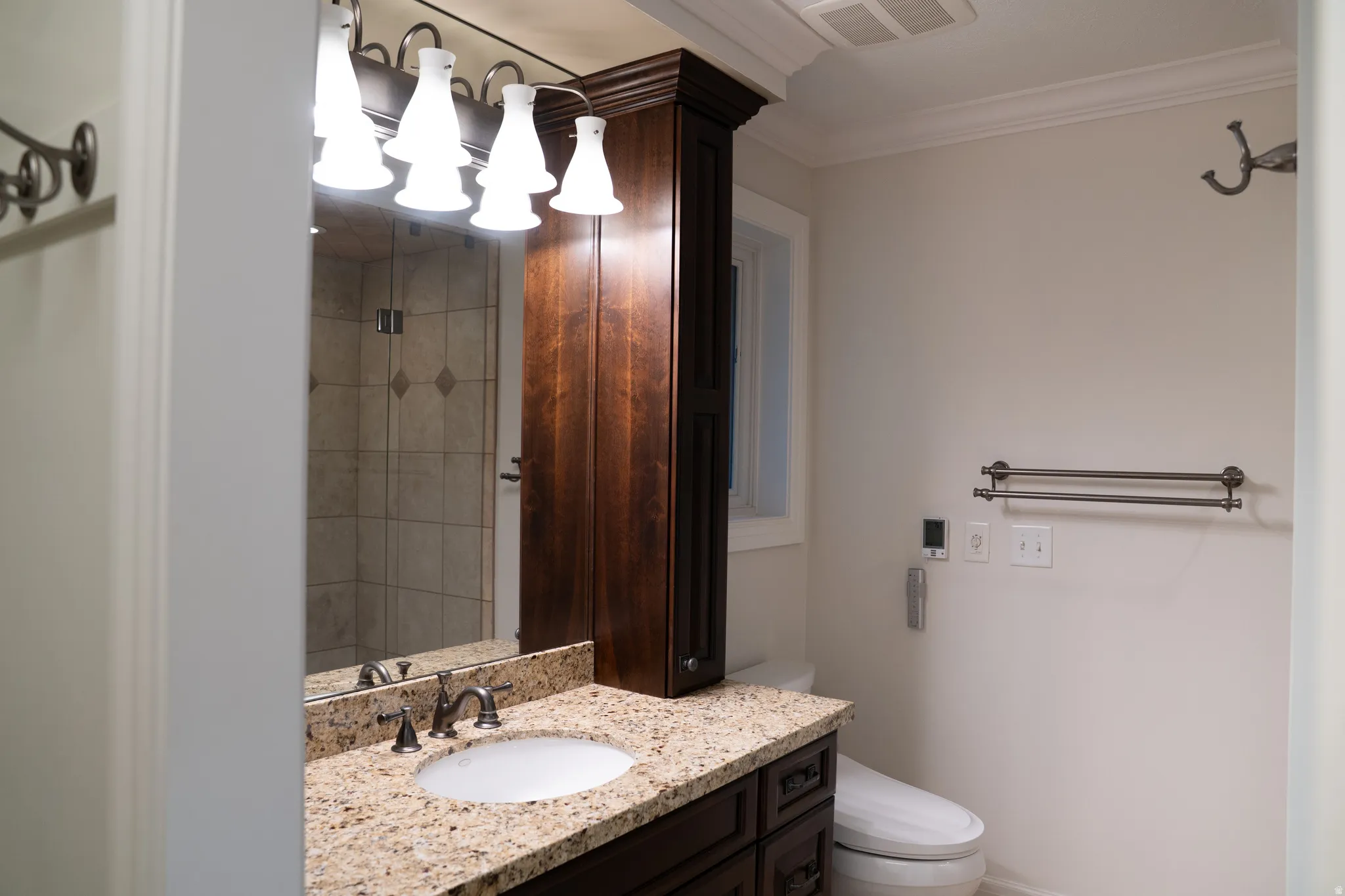 Granite-style countertop with undermount sink, dark wood-finish vanity, built-in storage cabinet, and tiled shower enclosure