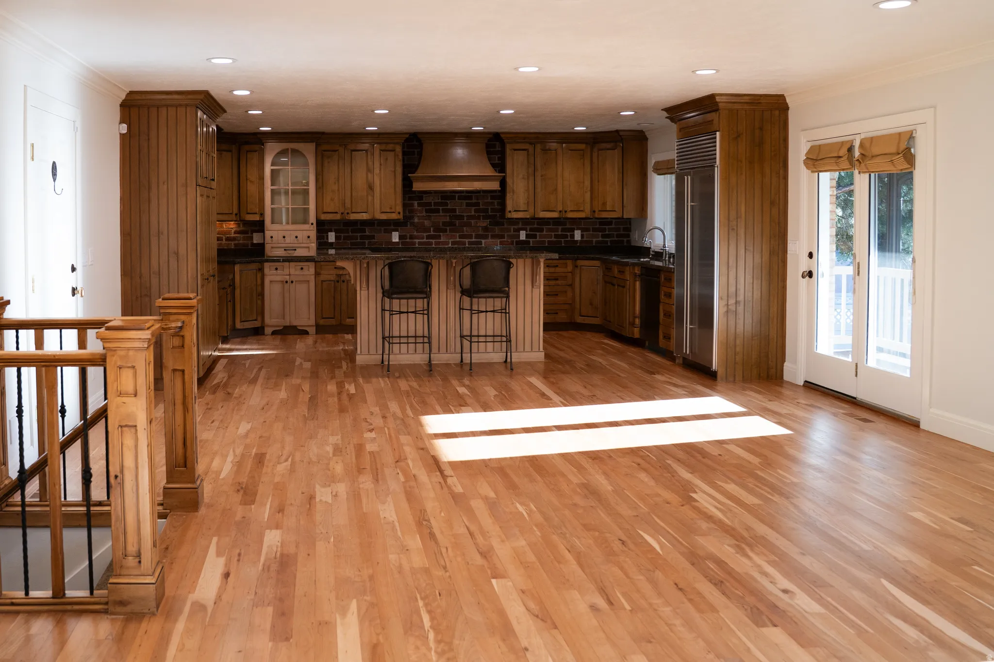Hardwood flooring extending into a kitchen with wood cabinetry, a brick-style backsplash, and recessed lighting