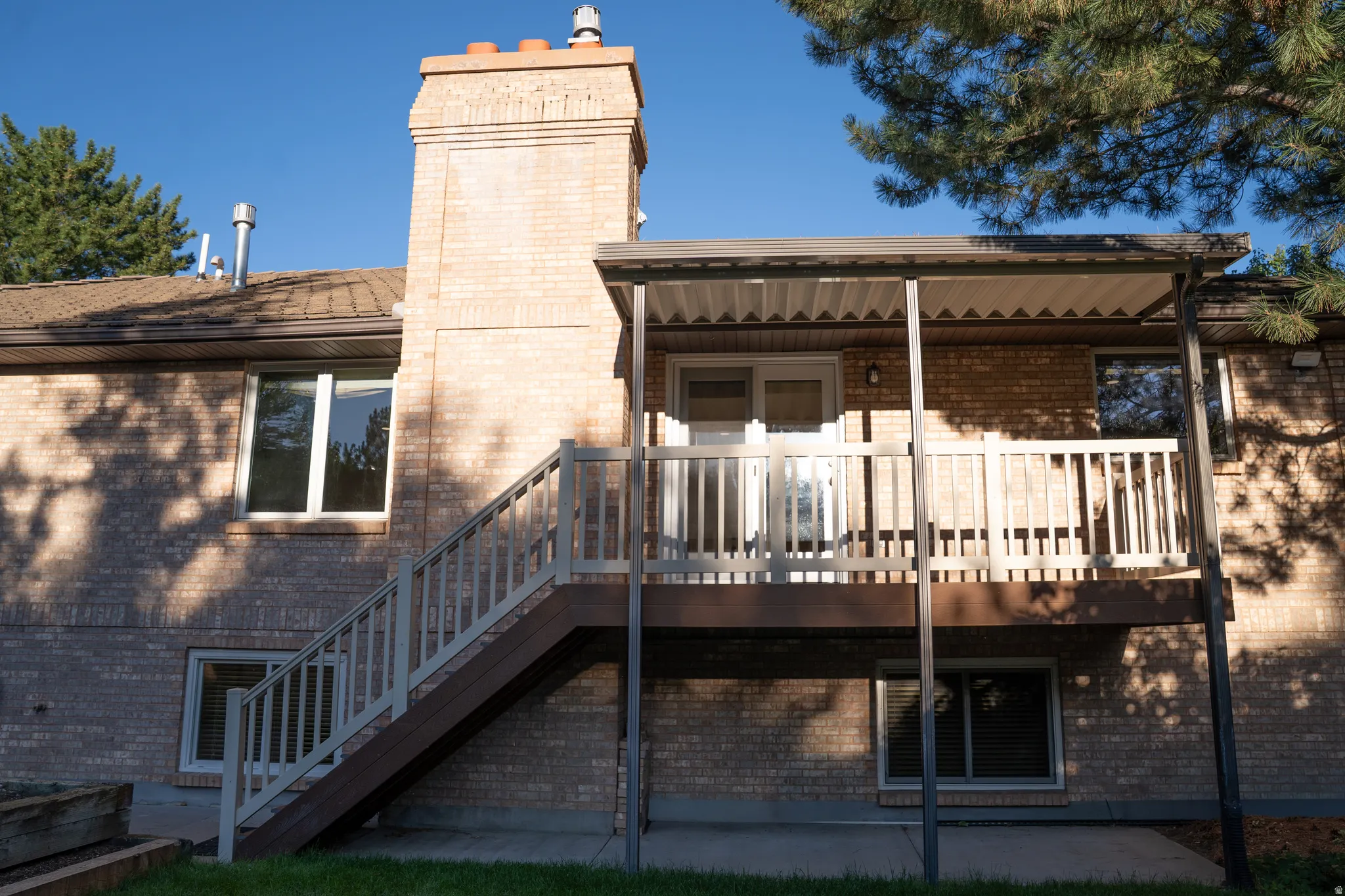 Brick exterior with a prominent chimney, elevated deck with white railing, covered patio area, and direct access via exterior stairs