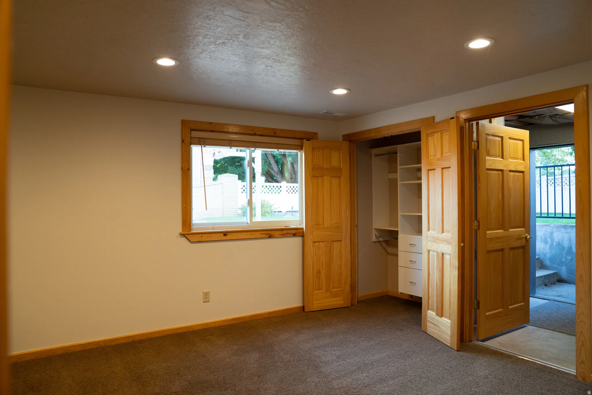 Recessed ceiling lighting, wood-trim window, built-in closet system with shelving and drawers, carpeted flooring, and a paneled wood door