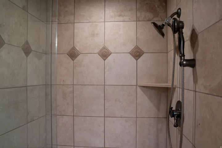 Tiled shower surround featuring decorative accent tiles and a built-in corner shelf