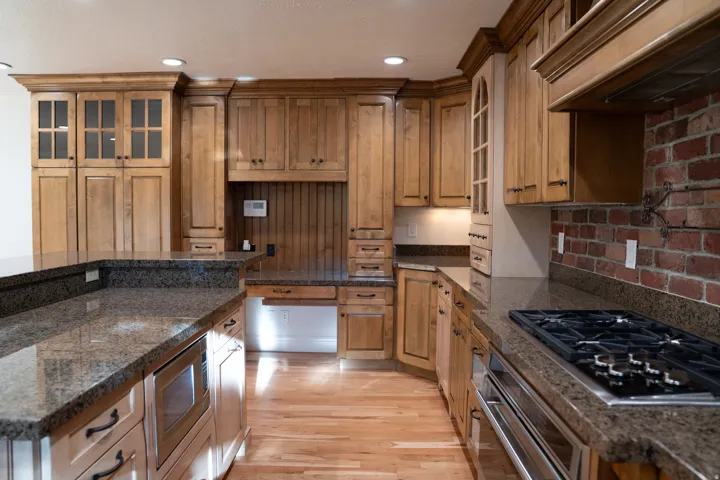 Wood-finish cabinetry with crown molding, dark granite countertops, hardwood flooring, brick-finish backsplash, and stainless steel appliances