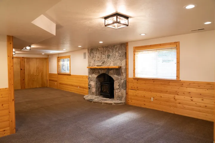 Stone-faced fireplace with wood mantel, wood paneling, recessed lighting, and a neutral carpeted floor