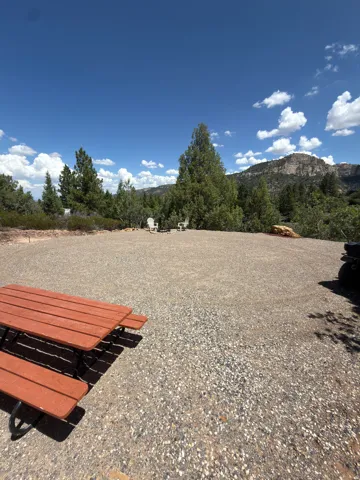 Gravel surface with a picnic table, featuring a natural tree line and mountain backdrop