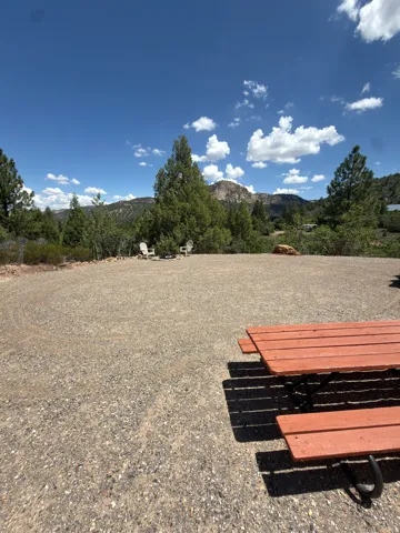 Gravel ground cover with a built-in fire pit, surrounded by mature trees, and distant mountainous terrain