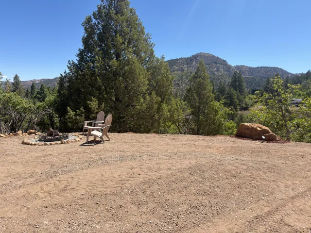 Gravel outdoor area featuring a stone-rimmed fire pit, surrounding trees, and distant mountainous terrain