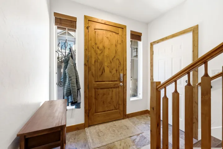 Wood-paneled entry door with sidelight windows, tile flooring, and wood stair railing